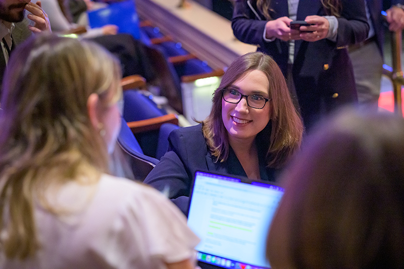 People inside an auditorium with a college student holding a laptop interviewing a political candidate.